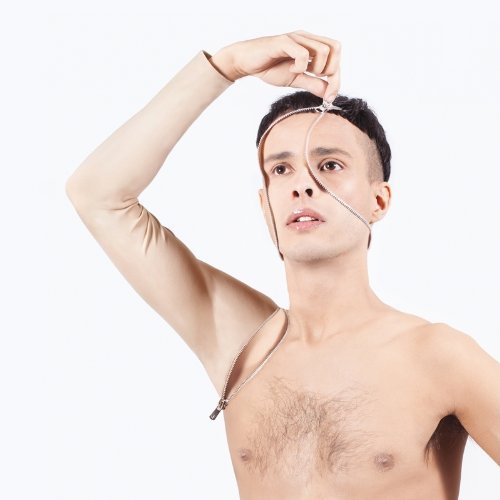 Man unzipping his face and torso, wearing a beige compression sleeve on his right arm.