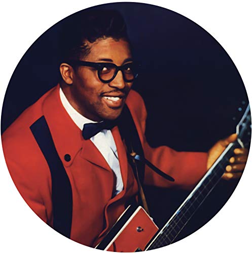 Man in red jacket playing guitar, wearing glasses and bow tie, circular image.