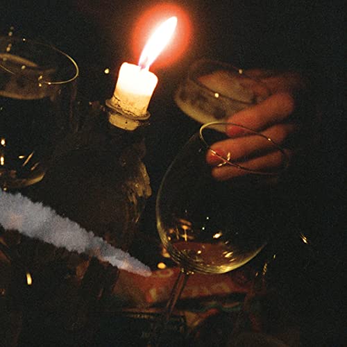 Candlelight illuminates wine glasses and a hand holding a cigarette.