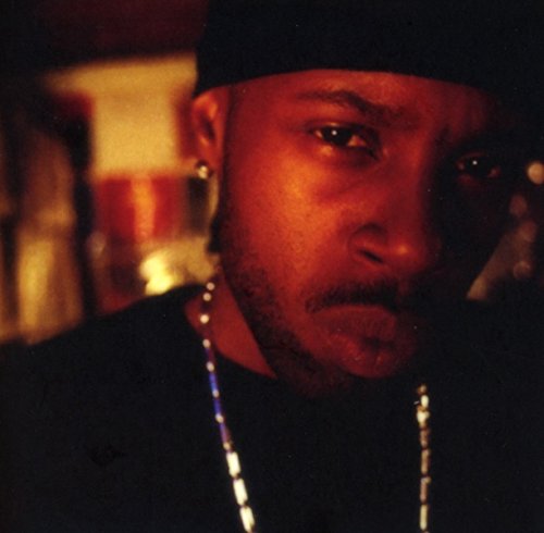 Close-up portrait of J Dilla, wearing a black cap and silver jewelry.