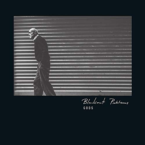"Album cover with a man in a suit walking past a shuttered storefront."