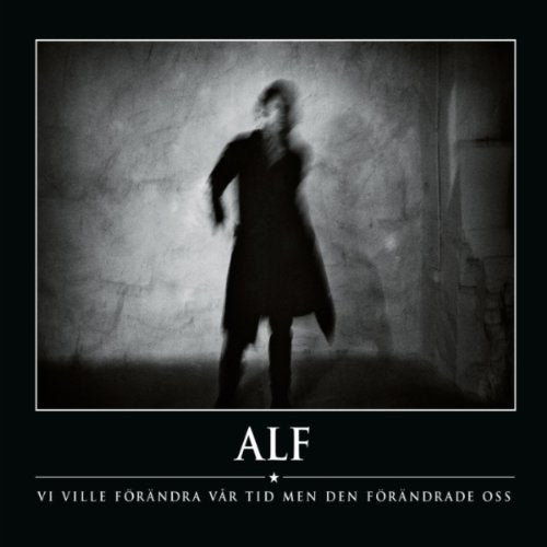 Blurred figure in a dark coat stands before a textured wall.
