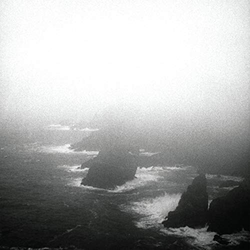 Black and white landscape of rocky coastline in dense fog.