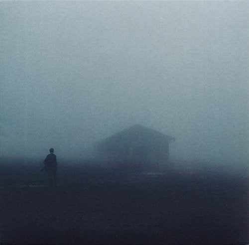 Dark, foggy landscape with a lone figure and small building.
