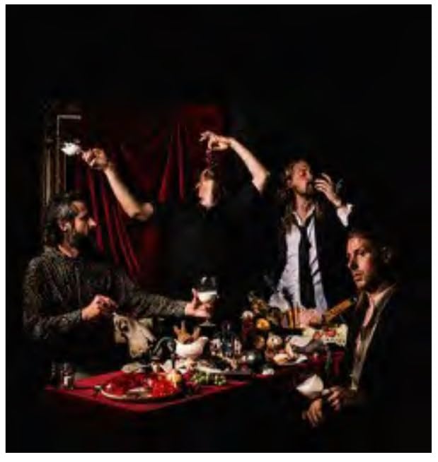 Four men in dark clothing sit around a red-clothed table with food and wine.