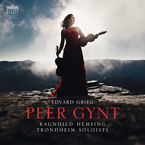 Woman in red dress with hardanger fiddle, mountainous landscape background.