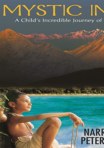 A young boy sits by a body of water with mountains in the background.