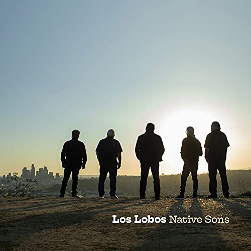 Silhouetted band Los Lobos stands on a hill overlooking a city skyline.