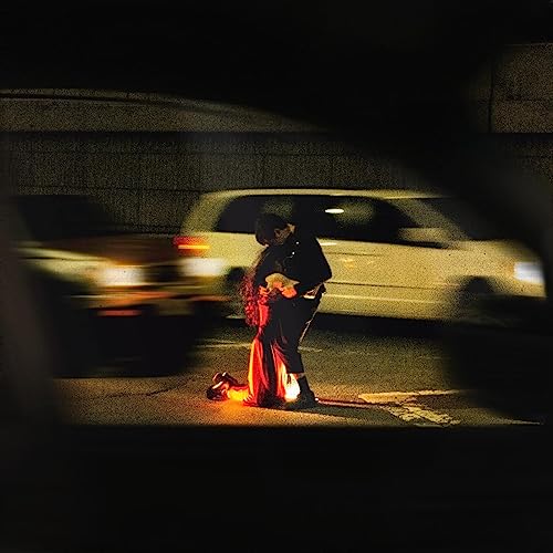 Person in dark clothing embracing someone in a red dress under an overpass.