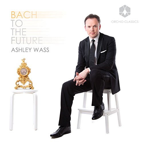 Man in a black suit sits on a white stool next to a gold clock.