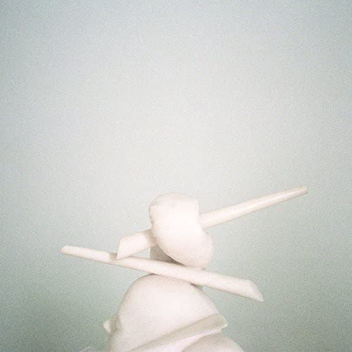 White abstract sculpture resembling a face and limbs on a pale background.