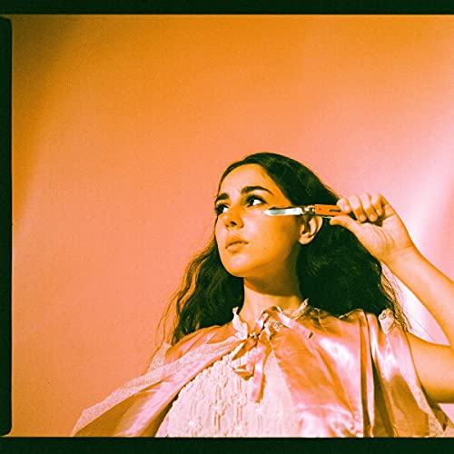 Woman with dark hair holds a pocketknife near her eye, orange background.