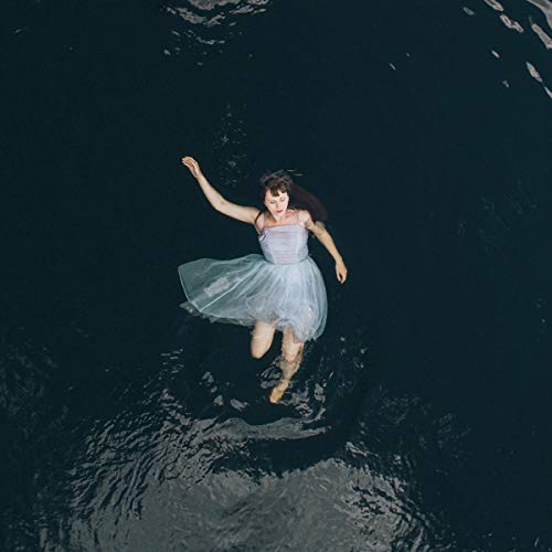 The alt text for the image is: "Woman in a white dress floating on dark water."