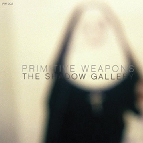 "Blurry album cover with 'Primitive Weapons' and 'The Shadow Gallery' text, dark figure in background."