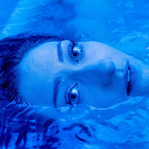 Blue-toned close-up of a person floating in water, eyes open.