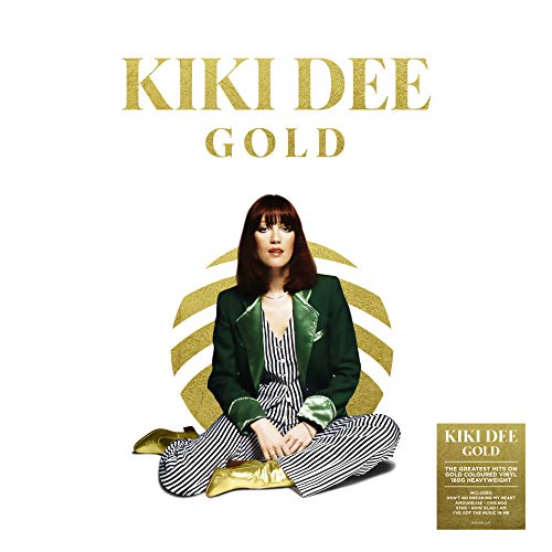 Kiki Dee sitting in a green jacket and striped trousers against a gold circle.
