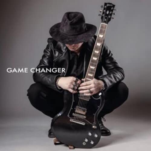 Man in hat crouching, playing a black electric guitar.