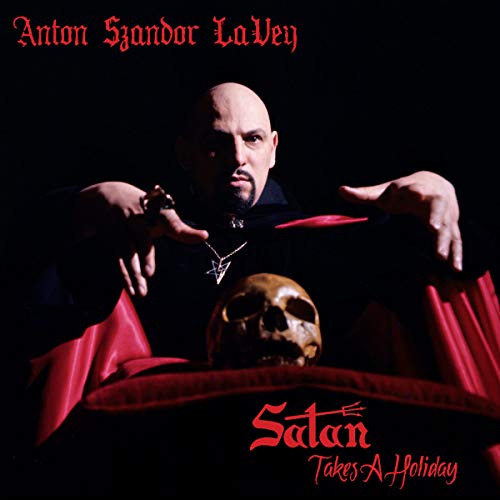 Anton LaVey holding a skull, wearing a black robe and pentagram pendant, against a dark background.