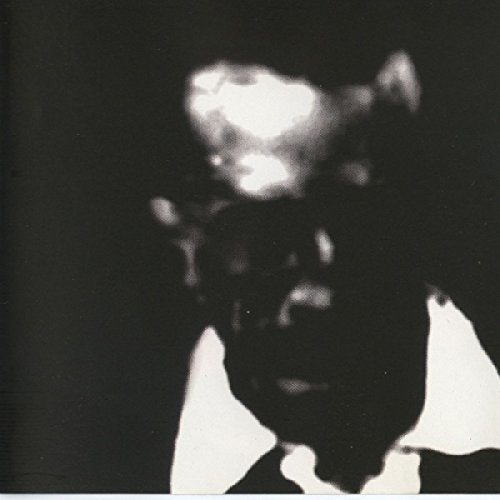 A blurry, black-and-white image of a man with a white shirt and dark face.