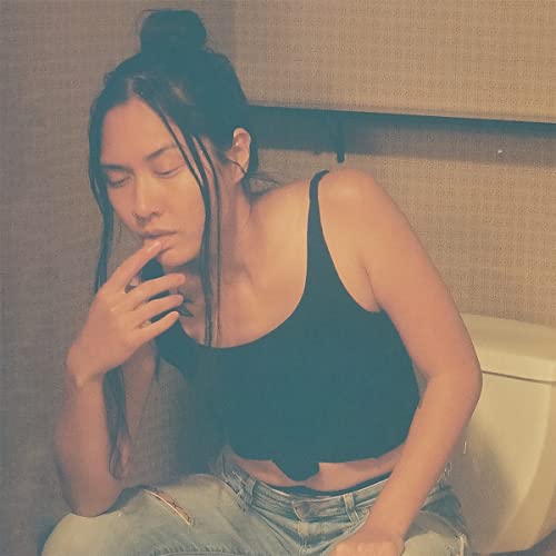 Woman with long dark hair sitting on a toilet, looking thoughtful.