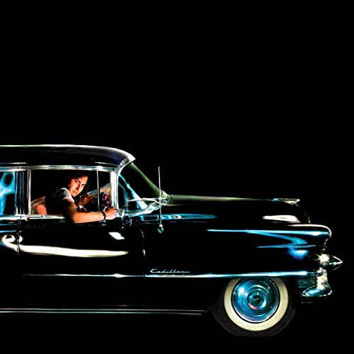 Man driving a classic, dark-colored 1955 Cadillac in low light.