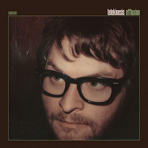 Close-up portrait of a man with brown hair and glasses on a brown background.