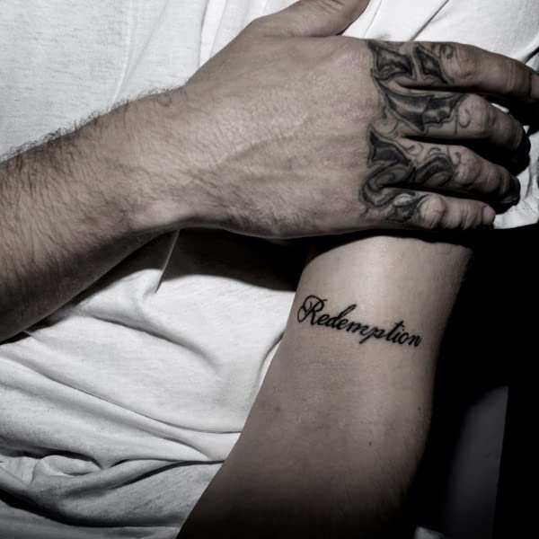 Arm with tattoos, including the word “Redemption” in cursive script.