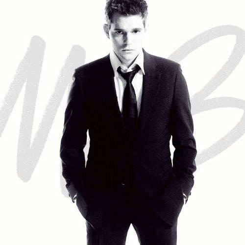 "Michael Bublé in a black suit, standing with hands in pockets, against a white background."