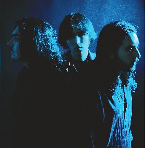 Blue-toned portrait of three long-haired men, likely a band, facing forward.