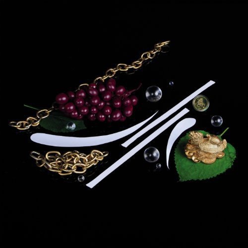 Still life with grapes, gold jewelry, white shapes, and green leaves on black.