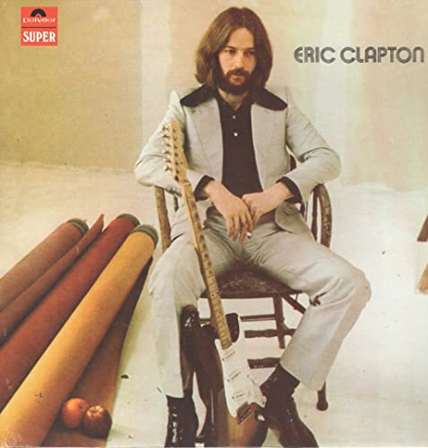 Eric Clapton album cover: man with guitar, seated near fabric rolls.