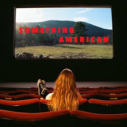 A woman sits alone in a cinema watching a film titled "Something American".