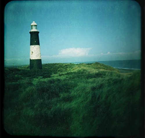 The image depicts a serene landscape with a lighthouse on a grassy hill. Alt text: Black and white lighthouse on a grassy hill with blue sky.