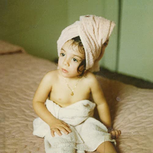 Young child with towel on head, sitting on a textured surface.