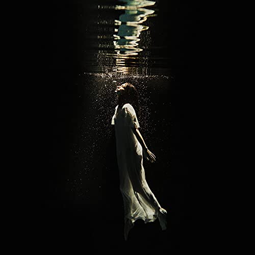 Woman in white dress submerged in dark water, bubbles rising.