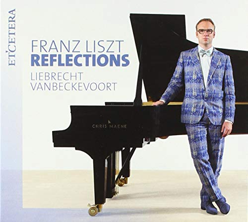 Man in blue suit standing beside a grand piano on a light background.