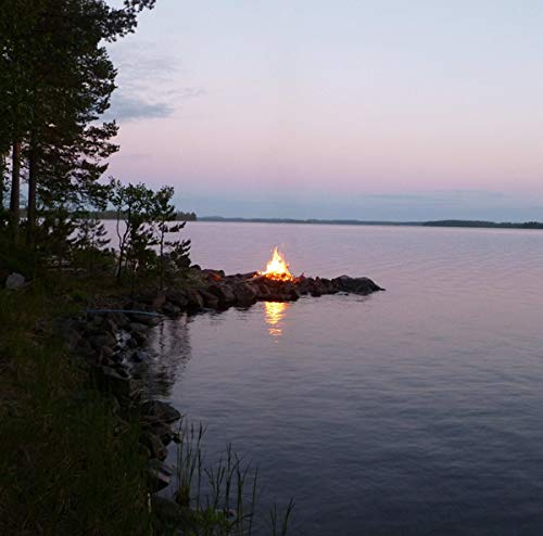 Bonfire burning on rocky shore at dusk, calm water, trees.