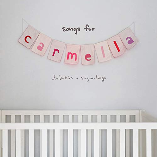 A banner spelling carmella hangs above a white crib against a light gray wall.