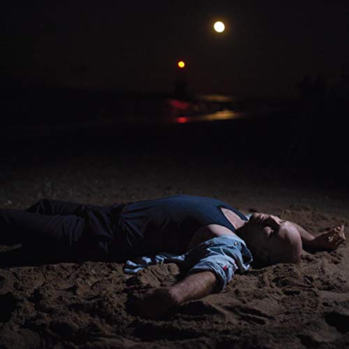 Person lying on dark sand beach under a moonlit sky.