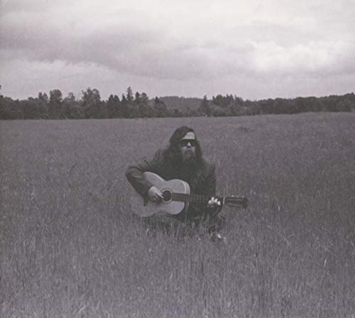 Black and white photo of a bearded man playing acoustic guitar in a field.