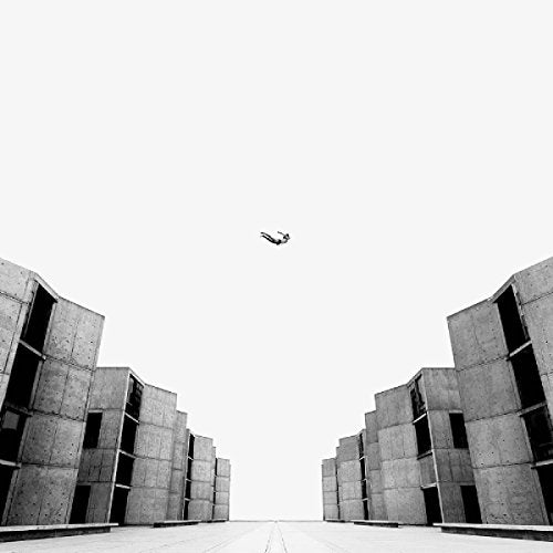 Black and white image of a person falling between concrete buildings.