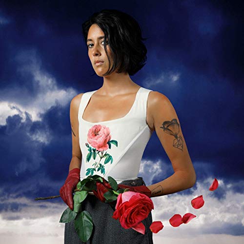 Woman in white tank top with rose design, holding roses, against a cloudy blue sky.