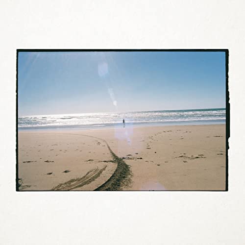 Beach scene with a lone figure walking towards the ocean.