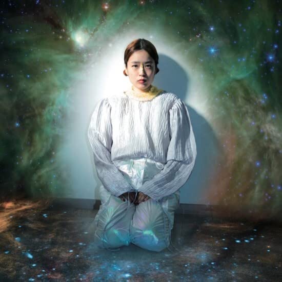 Woman kneeling against a cosmic, colorful nebula background.