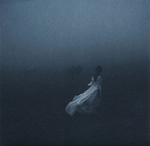 Woman in white dress standing in a foggy, dark landscape.
