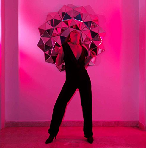 Woman in black jumpsuit holding a geometric mirrored shape, pink lighting.