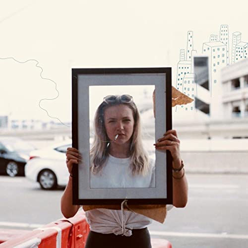 Woman holding a frame with a city skyline visible through it.