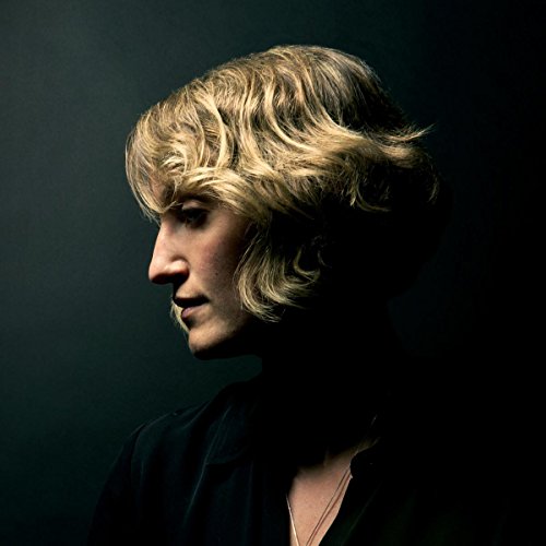Profile portrait of Joan Shelley with wavy blonde hair, dark background.