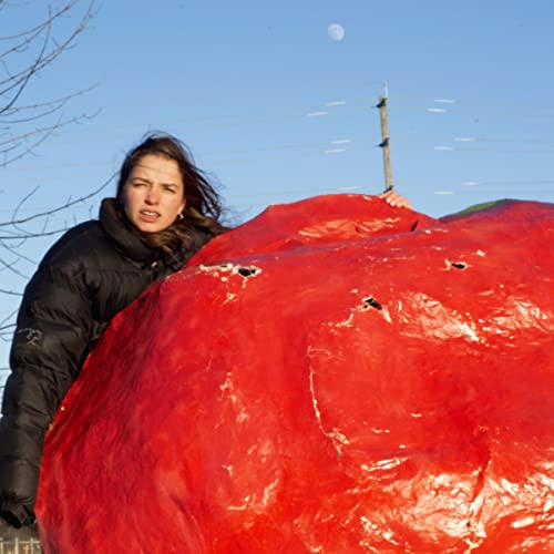 Woman struggles to hold a large, red, crumpled plastic shape outdoors.