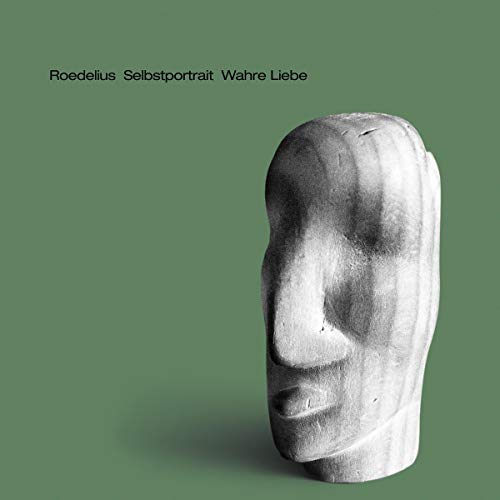 A stone sculpture of a face on a green background with black text above.